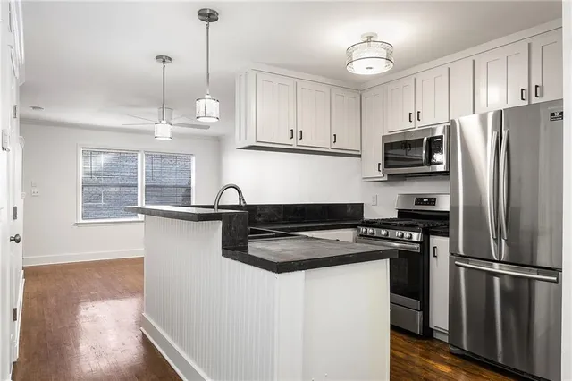 a kitchen with granite countertop a refrigerator a sink dishwasher a stove and white cabinets with wooden floor