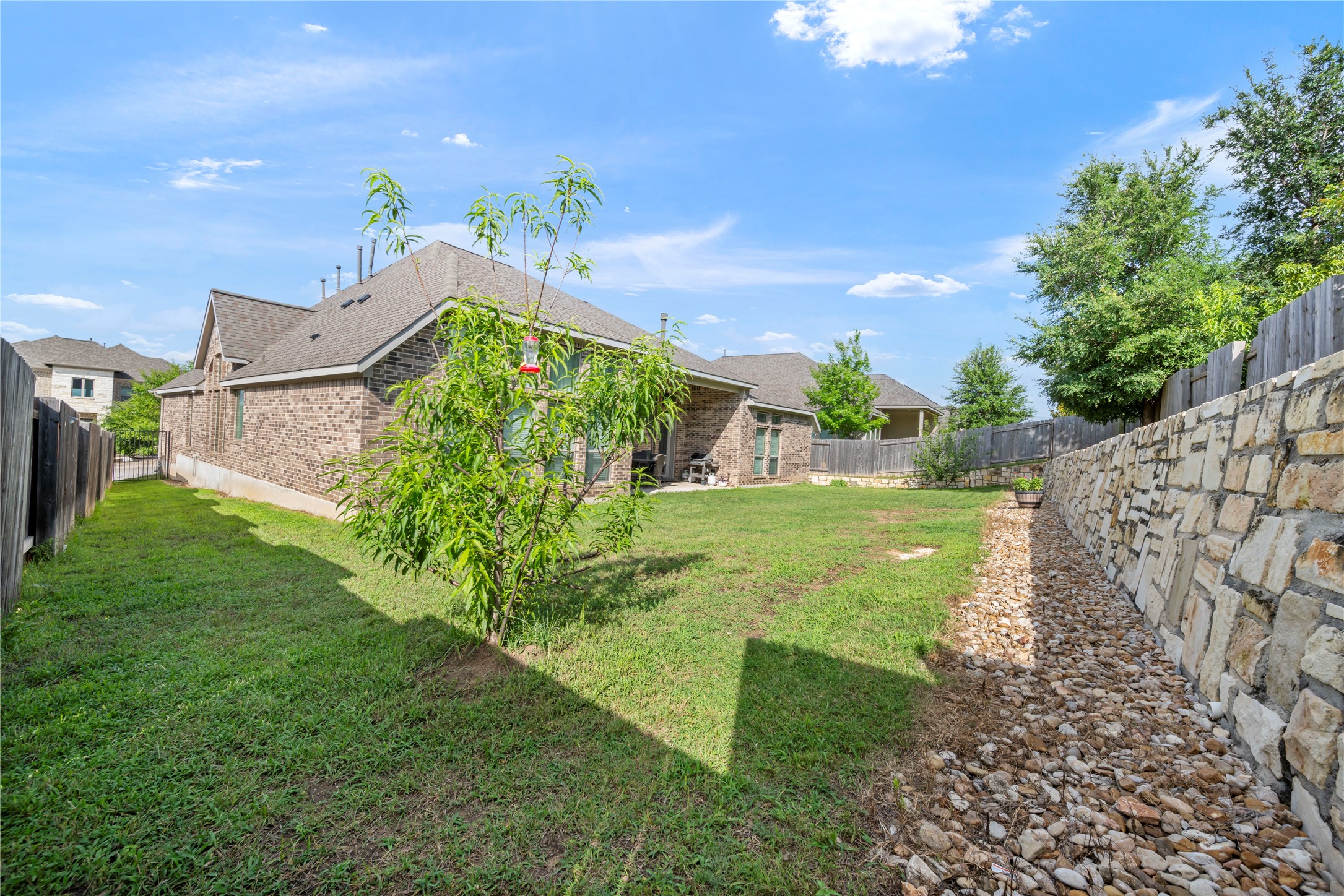 140 Catani Loop Georgetown, TX 78628 - Photo 34 of 36 A stone retaining wall gracefully lines the property, complemented by a verdant lawn and mature trees.