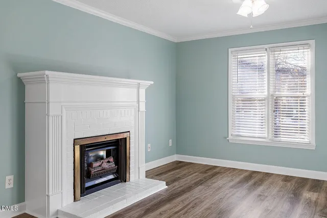 a view of an empty room with wooden floor fireplace and a window