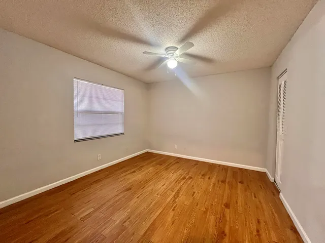 an empty room with wooden floor fan and windows