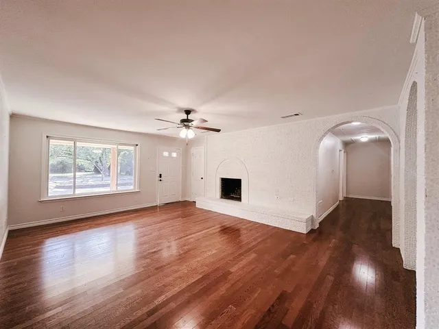 an empty room with wooden floor ceiling fan and window