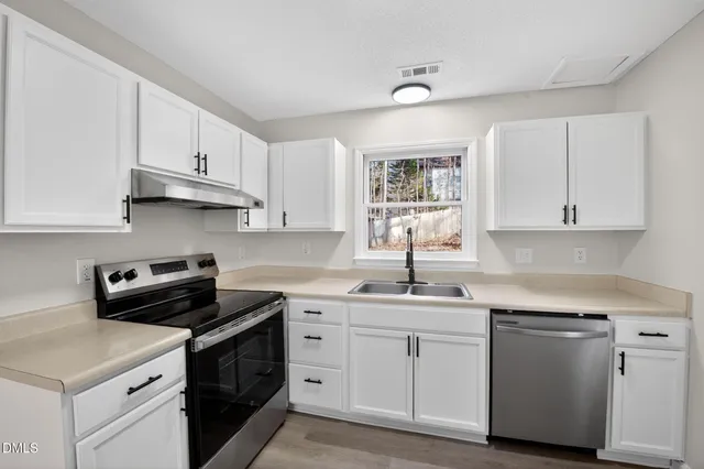 a kitchen with white cabinets appliances a sink and a window