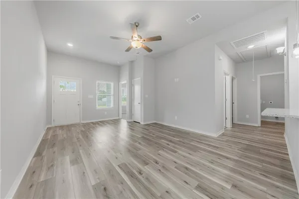 a view of an empty room with wooden floor and a ceiling fan