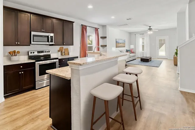 a kitchen with stainless steel appliances a sink a stove a refrigerator cabinets and a dining table