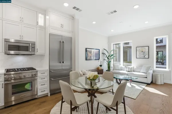 a kitchen with stainless steel appliances a stove a sink a microwave a refrigerator white cabinets and wooden floor