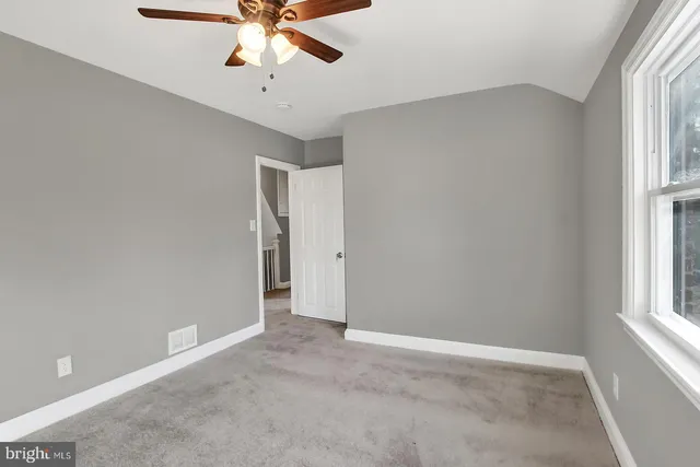 an empty room with chandelier fan and windows