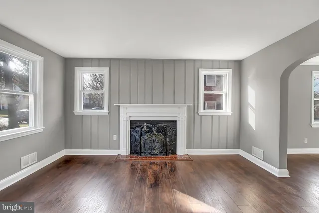 an empty room with wooden floor fireplace and windows
