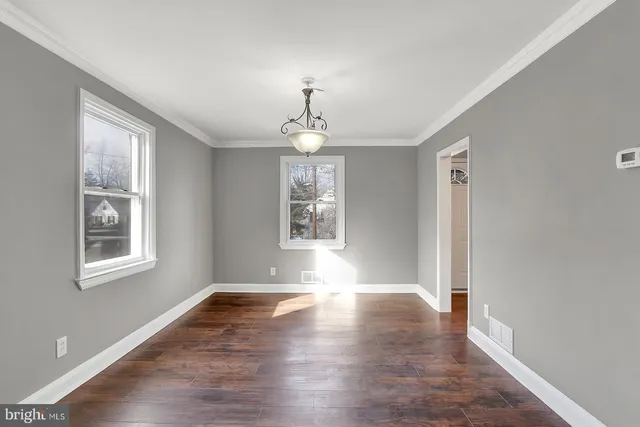 an empty room with wooden floor chandelier and windows