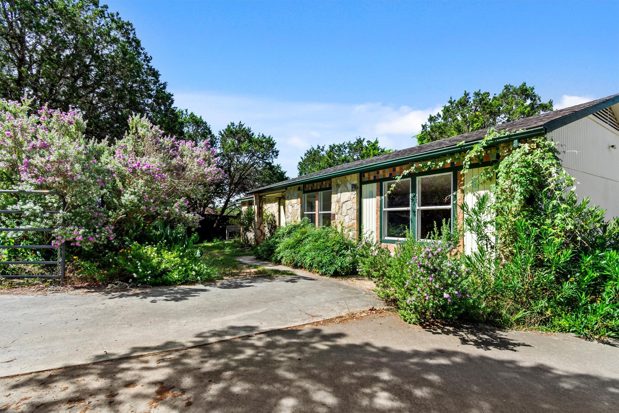 6 El Sol Road Wimberley, TX 78676 - Photo 1 of 20 Mature trees and vibrant shrubs surround this charming stone-clad home, offering natural shade and privacy.