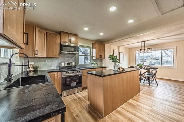 a kitchen with stainless steel appliances granite countertop a stove top oven a sink dishwasher a dining table and chairs with wooden floor