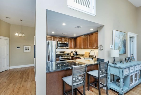 52 Sanborn Street, Unit 102 Reading, MA 01867 - Photo 8 of 28 a kitchen with stainless steel appliances kitchen island granite countertop a stove a refrigerator a sink a dining table and chairs with wooden floor