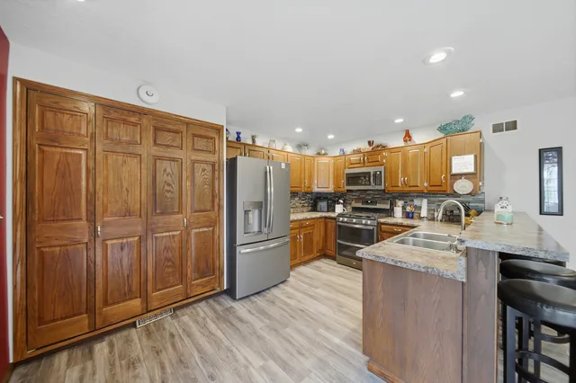 a kitchen with stainless steel appliances granite countertop a refrigerator a sink dishwasher and wooden cabinets with wooden floor