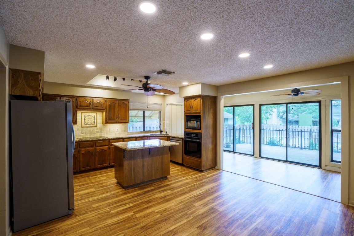 a open kitchen with stainless steel appliances granite countertop a refrigerator a sink dishwasher a oven and a large countertops with wooden floor