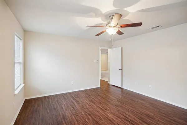 an empty room with wooden floor fan and windows