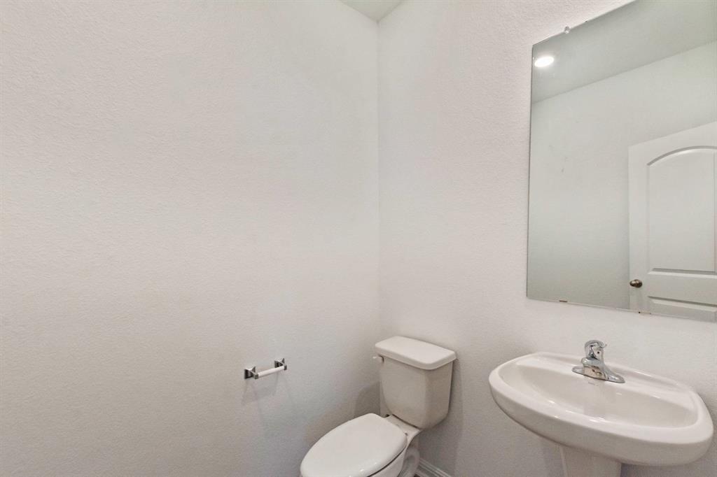 16429 Farmhouse Lane Elgin, TX 78621 - Photo 15 of 22 Pedestal sink with chrome faucet, a rectangular wall-mounted mirror, and a toilet with an adjacent toilet paper holder