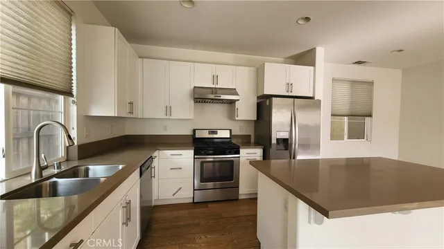a kitchen with stainless steel appliances granite countertop a sink dishwasher a refrigerator and cabinets with wooden floor