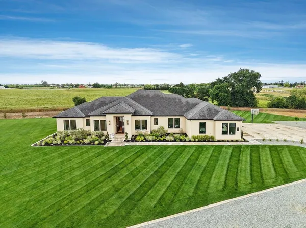 a view of a white house with a big yard potted plants and large tree