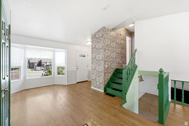 2475 Church Street Layton, UT 84040 - Photo 9 of 27 Bright entryway featuring wood-finish flooring, a bay window with natural light, a textured accent wall, and a staircase with green railings