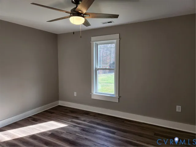 an empty room with wooden floor fan and windows
