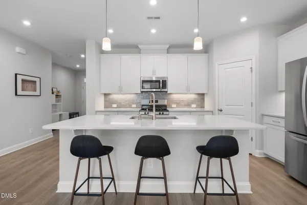 a kitchen with stainless steel appliances a dining table chairs refrigerator and cabinets