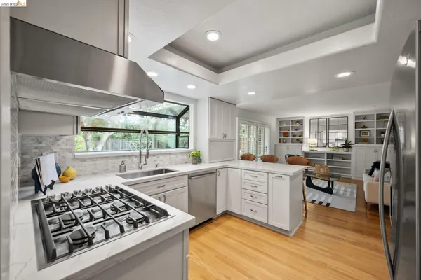 a kitchen with stainless steel appliances granite countertop a stove top oven a sink dishwasher and white cabinets with wooden floor
