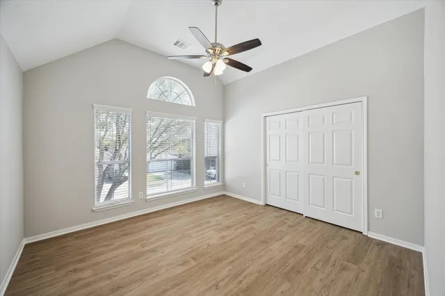 an empty room with wooden floor fan and windows