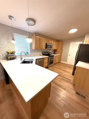 a kitchen with stainless steel appliances a sink a stove a refrigerator white cabinets a dining table and chairs