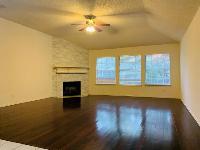 a view of an empty room with wooden floor fireplace and a window