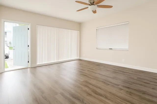 an empty room with wooden floor fan and windows