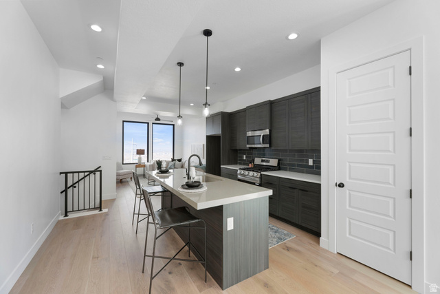 14392 South Champ Cove Draper, UT 84020 - Photo 6 of 31 Kitchen with a kitchen bar, a kitchen island with sink, stainless steel appliances, modern cabinets, and light wood finished floors