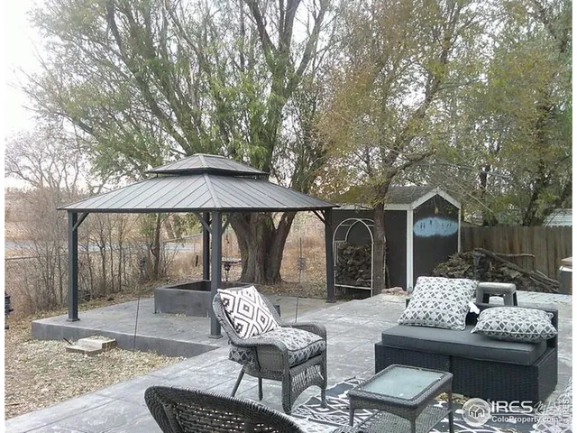 a view of a patio with couches table and chairs under an umbrella with large trees