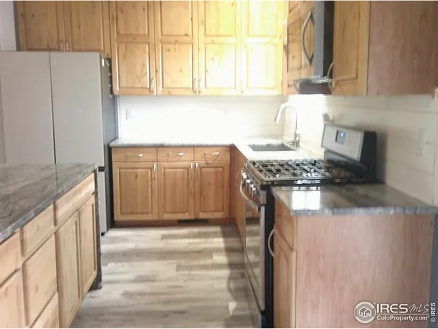 a kitchen with stainless steel appliances granite countertop a refrigerator a stove and a sink with wooden cabinets