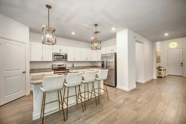 a kitchen with stainless steel appliances kitchen island granite countertop a refrigerator a stove top oven a sink dishwasher and white cabinets with wooden floor