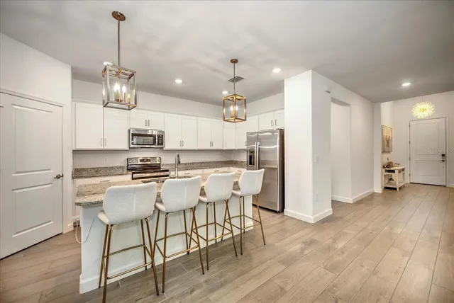 a kitchen with stainless steel appliances kitchen island granite countertop a refrigerator a stove top oven a sink dishwasher and white cabinets with wooden floor