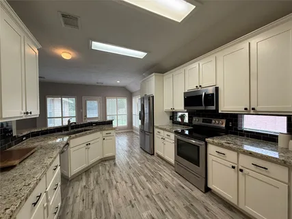 a view of a kitchen with stainless steel appliances granite countertop a stove a sink dishwasher and a microwave oven with cabinets