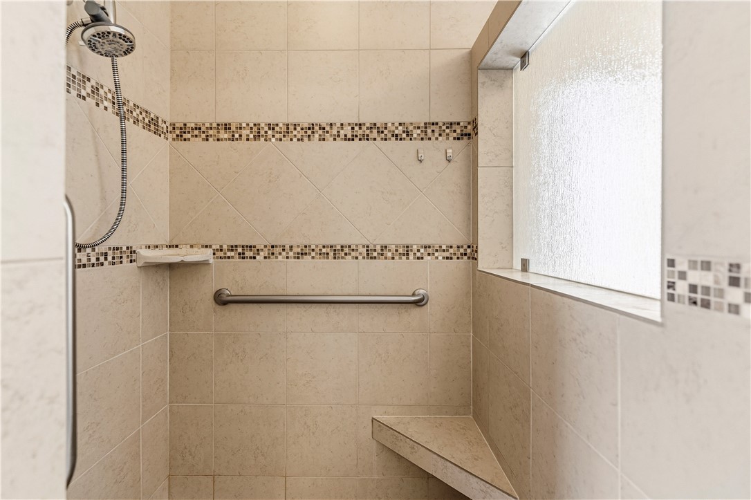 3315 Rainbow Mine Road Kingman, AZ 86401 - Photo 24 of 54 Shower with neutral-toned tiled walls, decorative mosaic tile accents, a built-in corner bench, and a frosted window