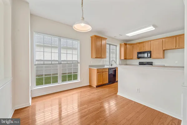 a kitchen with stainless steel appliances granite countertop a stove a sink a refrigerator white cabinets and wooden floor next to a window