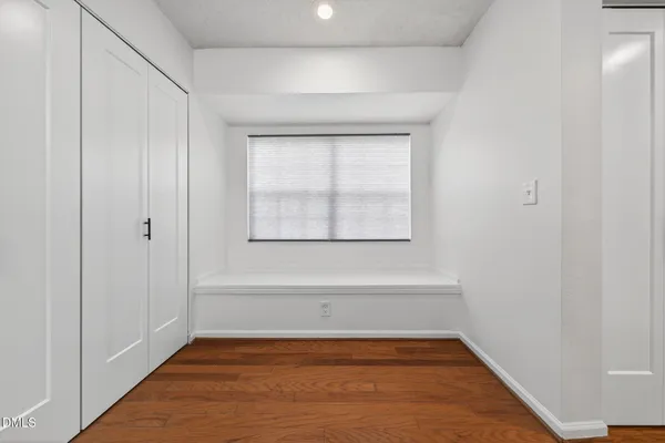 a view of an empty room with wooden floor and a window