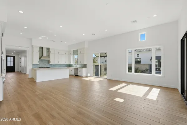 a view of an empty room with wooden floor and a kitchen