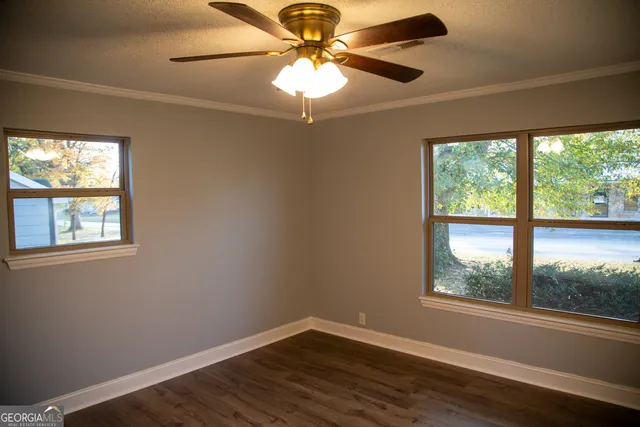 an empty room with wooden floor chandelier fan and windows