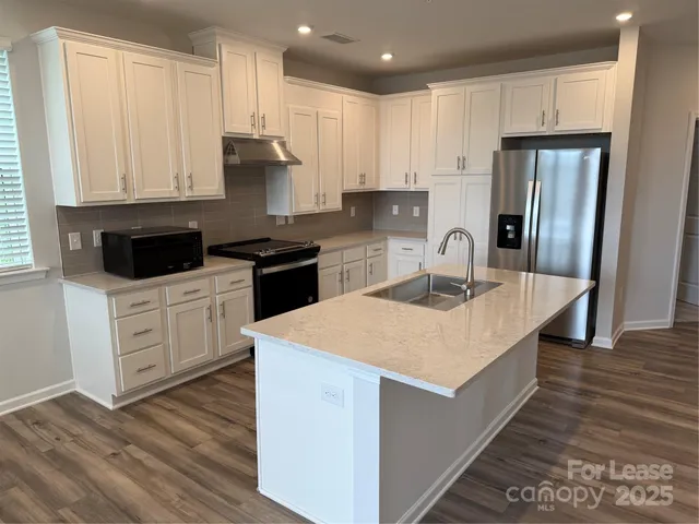 a kitchen with stainless steel appliances granite countertop a stove a sink dishwasher and a refrigerator with wooden floor