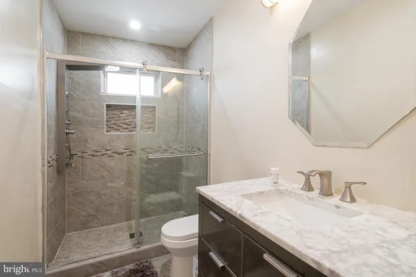 a bathroom with a granite countertop sink a toilet a mirror and shower