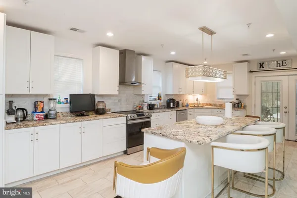 a kitchen with stainless steel appliances granite countertop a sink a stove a kitchen island with chairs and white cabinets