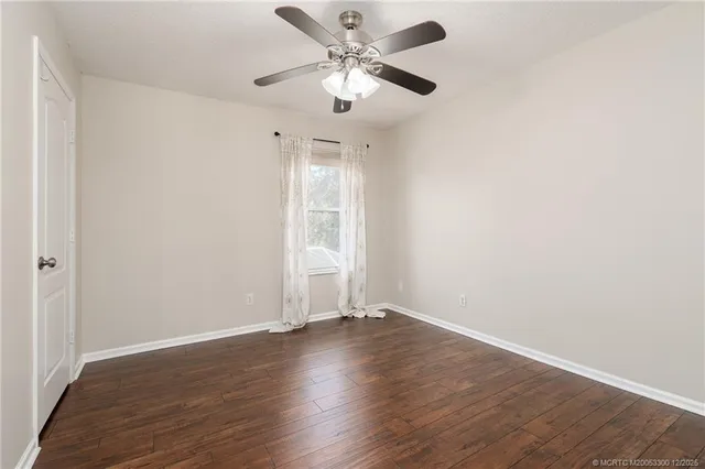 an empty room with wooden floor ceiling fan and window