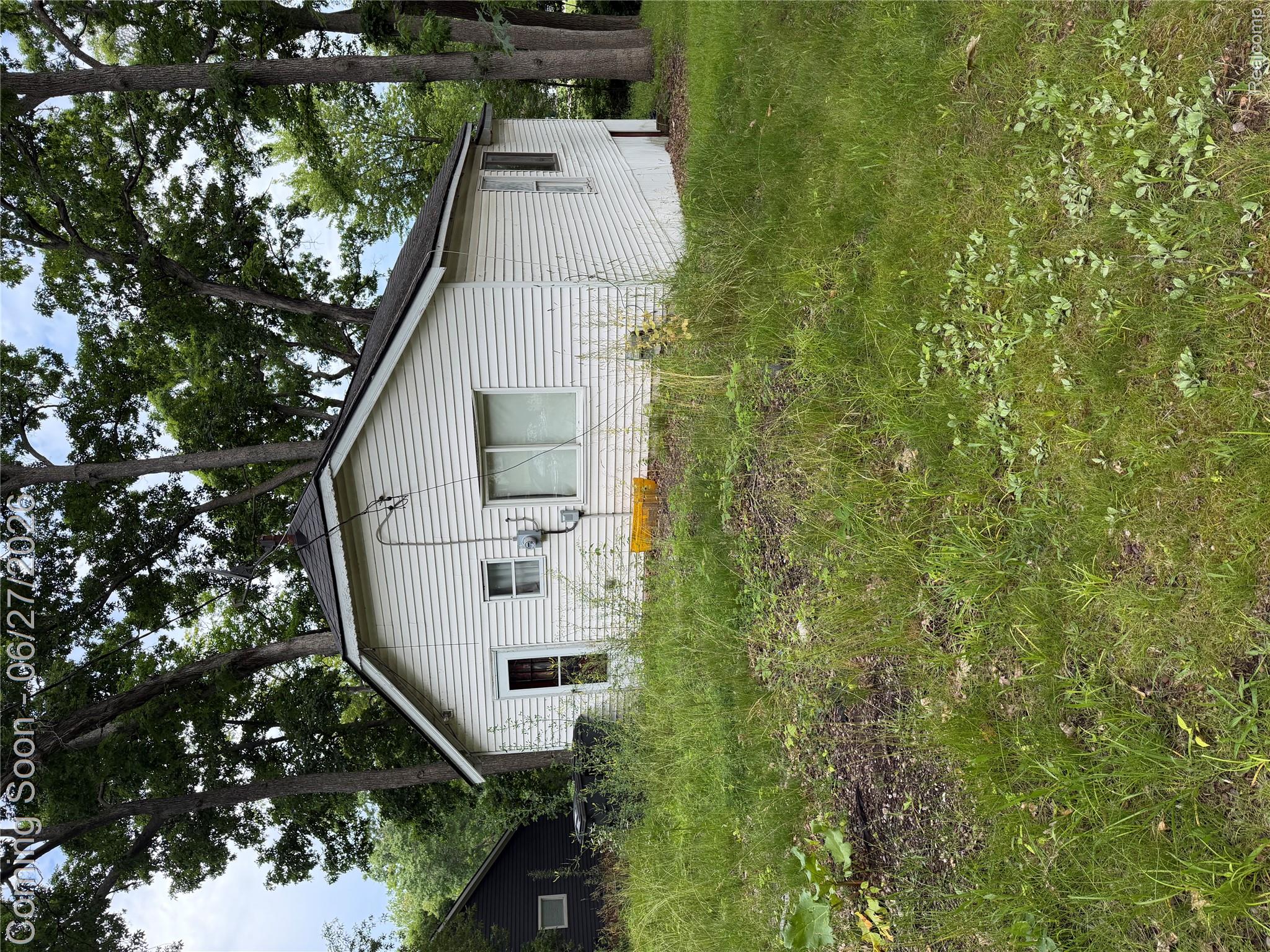 White siding exterior with a dark shingle roof and mature trees surrounding the property