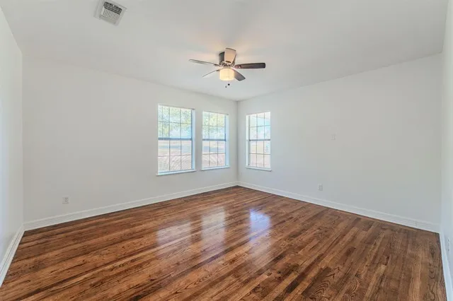 an empty room with wooden floor ceiling fan and windows