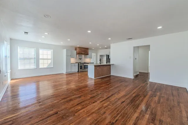 a view of an empty room with wooden floor and a kitchen