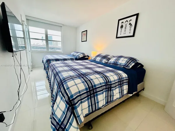 a bedroom with a bed next to a window with a flat tv screen and a dresser