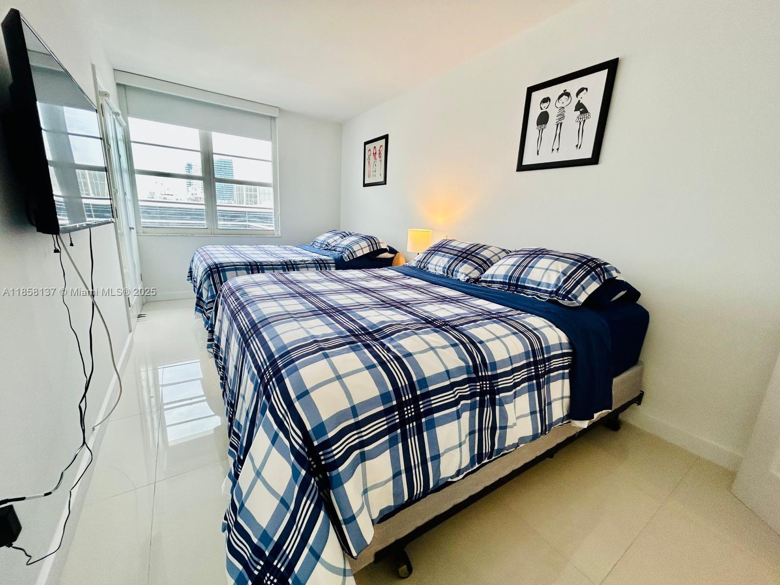 100 Lincoln Road, Unit 1406 Miami Beach, FL 33139 - Photo 9 of 14 a bedroom with a bed next to a window with a flat tv screen and a dresser