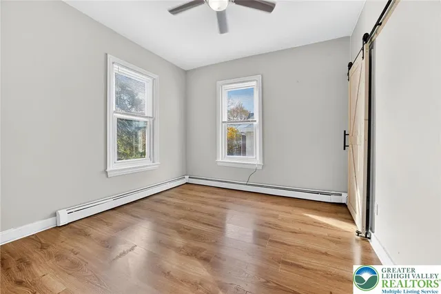 an empty room with wooden floor chandelier fan and windows